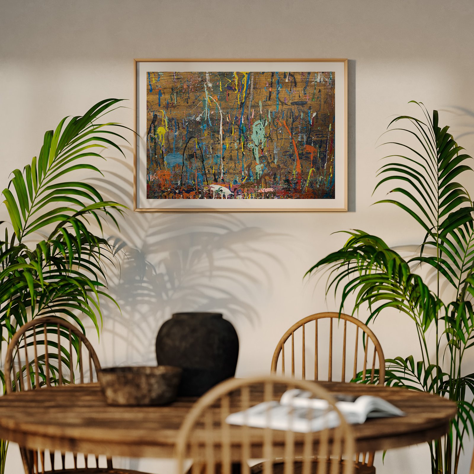 Horizontal abstract street art photograph with bold blue, yellow, red, and cyan paint marks on a textured yellow-gold background in a natural wood frame, hung on a cream wall above a wooden dining table, styled with potted palm plants flanking the composition and dining chairs visible below.