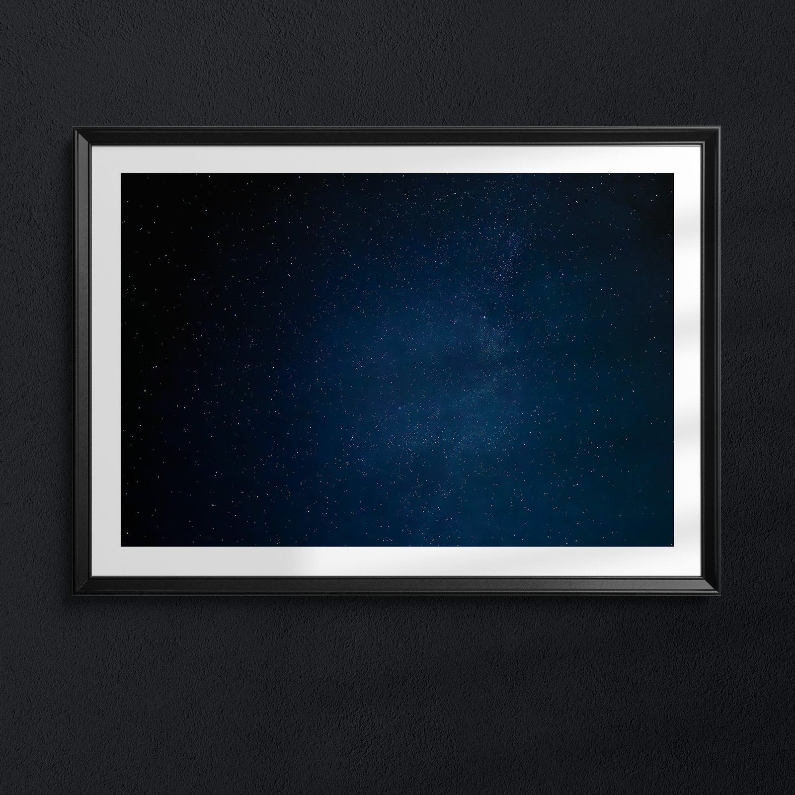 Horizontal night sky photograph with deep blue atmosphere and scattered stars in a black frame with white double mat, hung on a dark charcoal wall, creating a dramatic framed presentation against the moody background.