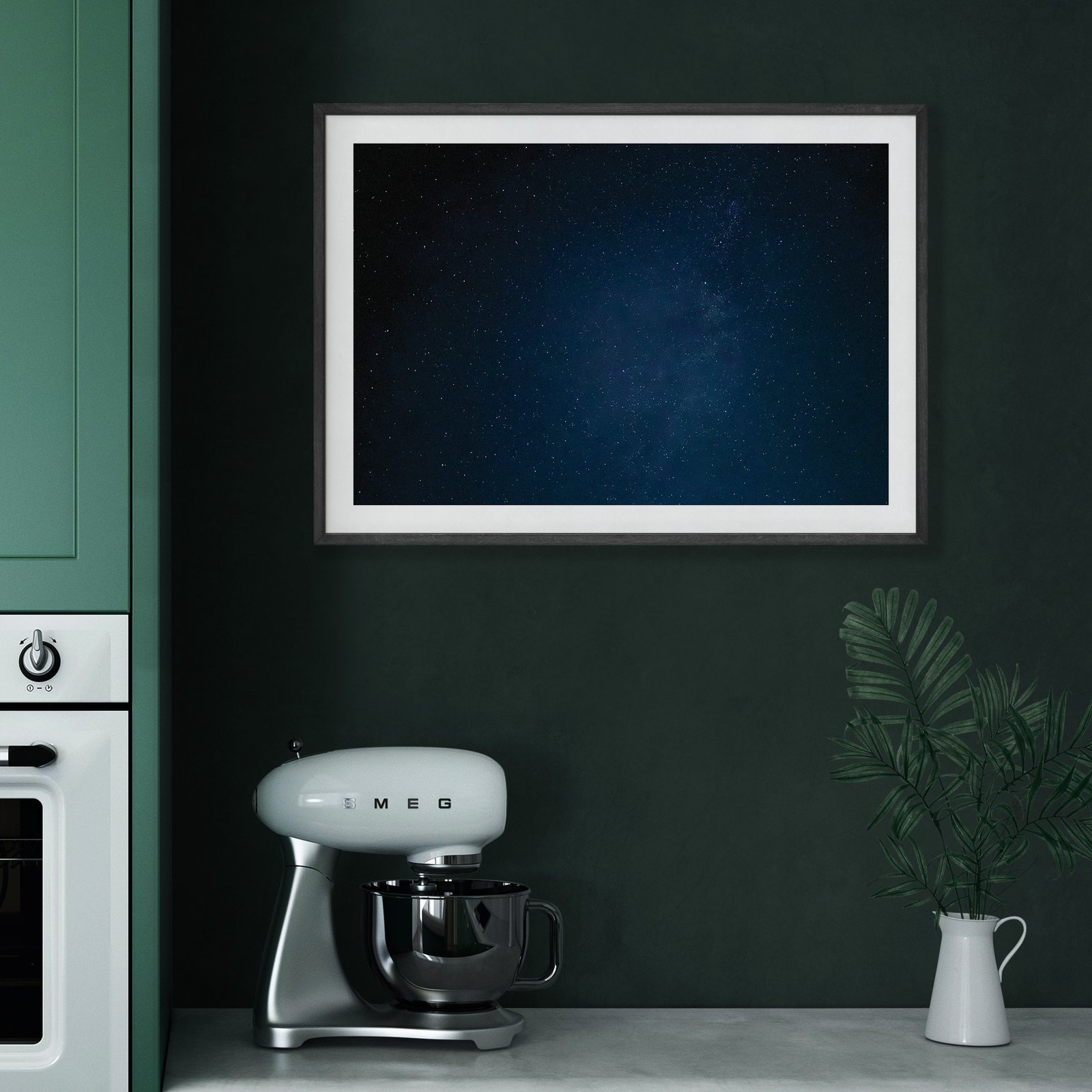 Horizontal night sky photograph with deep blue tones and stars visible in a white frame, hung on a rich dark green kitchen wall above a vintage cream and black retro coffee maker (SMEG style), styled with a white ceramic pitcher.